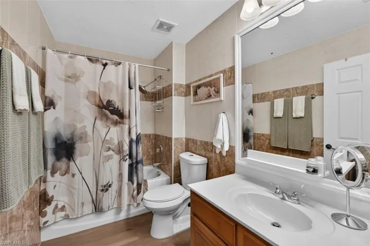 Full bath featuring shower / bathtub combination with curtain, vanity, tile walls, and light wood-style flooring