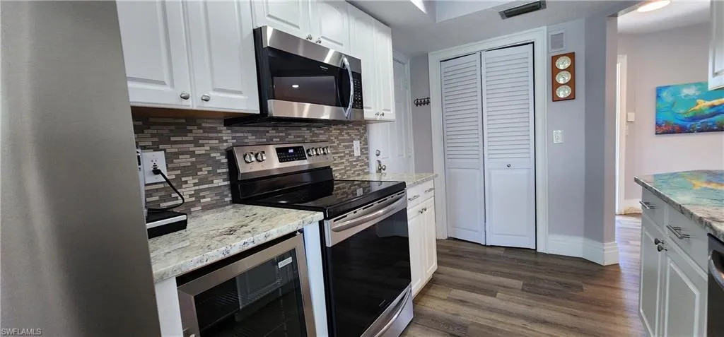 Kitchen featuring light stone countertops, dark wood-type flooring, appliances with stainless steel finishes, white cabinets, and backsplash