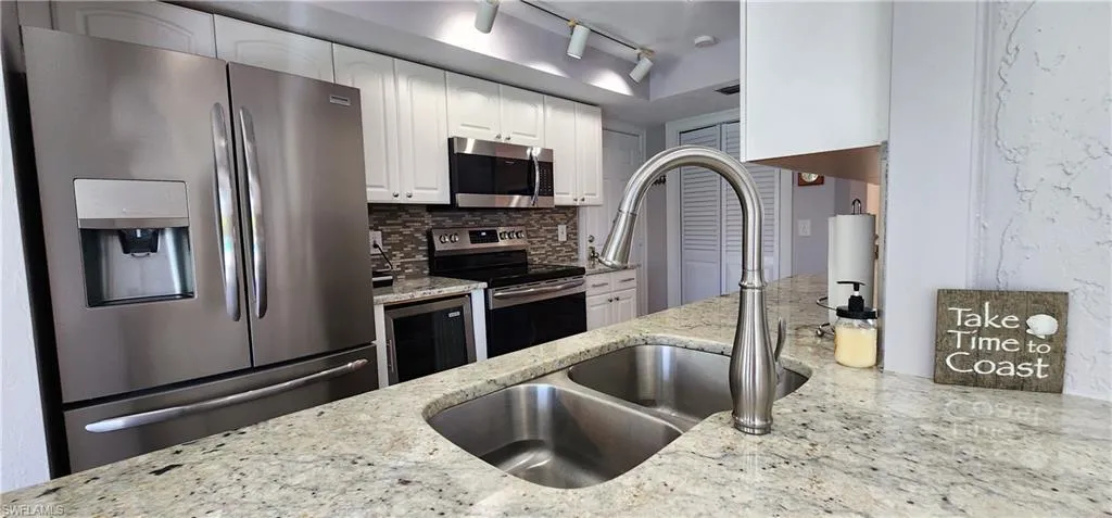 Kitchen featuring light stone countertops, appliances with stainless steel finishes, white cabinets, backsplash, and track lighting