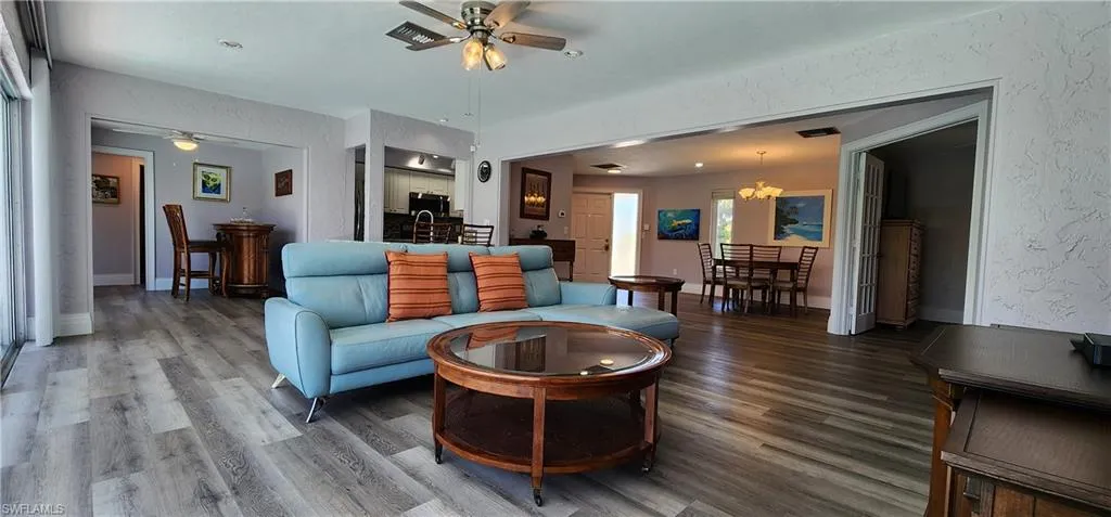 Living room featuring ceiling fan with notable chandelier, wood-style floors, and sink