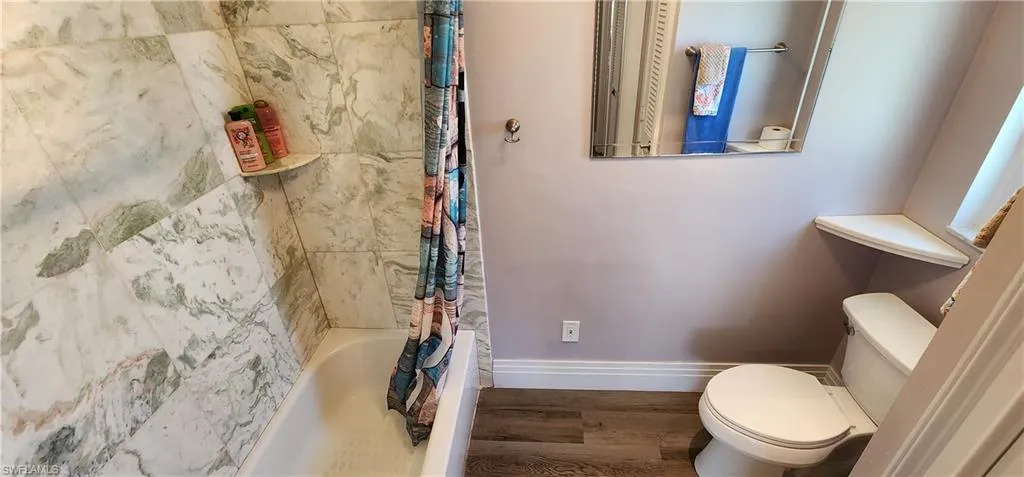 Bathroom with shower / bath combo with shower curtain, toilet, and wood-style floors