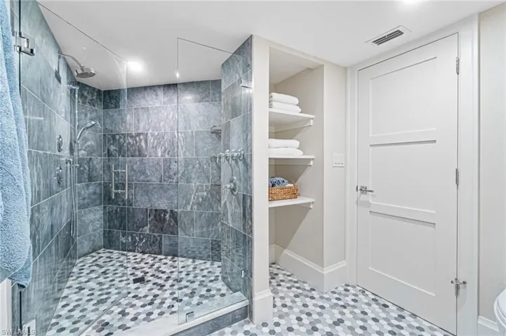 Primary bathroom features a large walk in shower with custom tile, multiple shower heads and a frameless shower door.