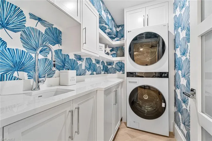 Laundry room is tucked away behind a privacy door and features custom wallpaper, sink, storage space and stacked washer and dryer