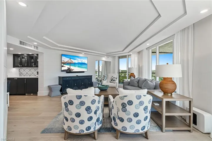 Living room features a raised ceiling, recessed lighting, and light wide plank hardwood floors and access to the balcony