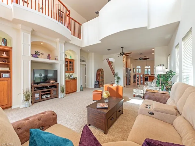 Carpeted living room with ceiling fan, built in features, and a towering ceiling