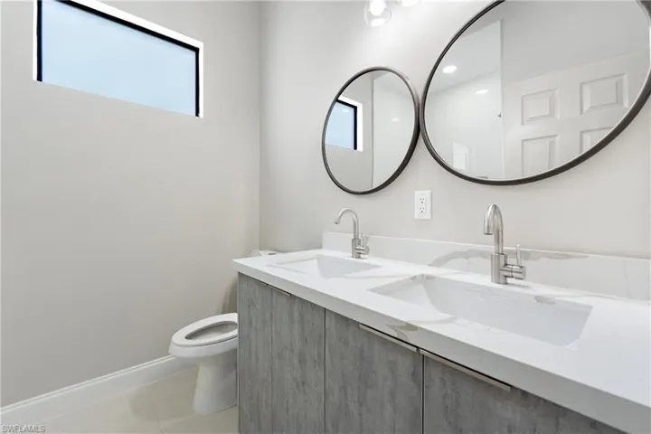 Full bathroom featuring double vanity, light tile patterned floors, and plenty of natural light