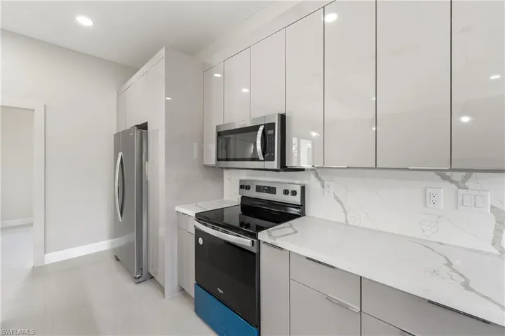 Kitchen featuring appliances with stainless steel finishes, modern cabinets, light stone counters, backsplash, and recessed lighting