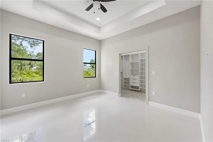 Unfurnished bedroom with a tray ceiling, a walk in closet, ceiling fan, light tile patterned flooring, and recessed lighting
