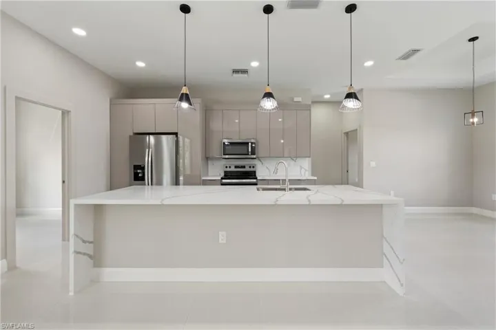 Kitchen featuring appliances with stainless steel finishes, light stone countertops, modern cabinets, a large island with sink, and decorative light fixtures