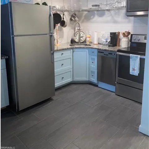 Kitchen with stainless steel appliances, light stone counters, wood tiled floors, and decorative backsplash