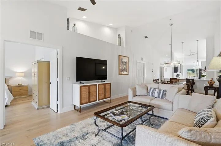 Living room featuring light wood finished floors, ceiling fan, suspended lighting, and vaulted ceiling