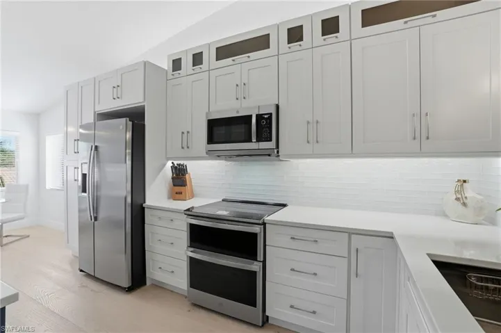 Kitchen with stainless steel appliances, light wood-style flooring, decorative backsplash, vaulted ceiling, and light stone countertops