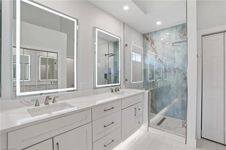 Full bath featuring double vanity, a marble finish shower, light tile patterned floors, and recessed lighting