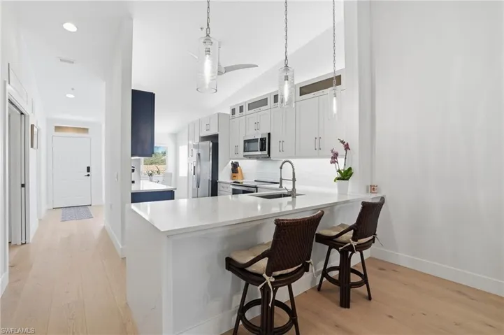 Kitchen featuring a breakfast bar area, a peninsula, vaulted ceiling, light wood finished floors, and glass fronted cabinets