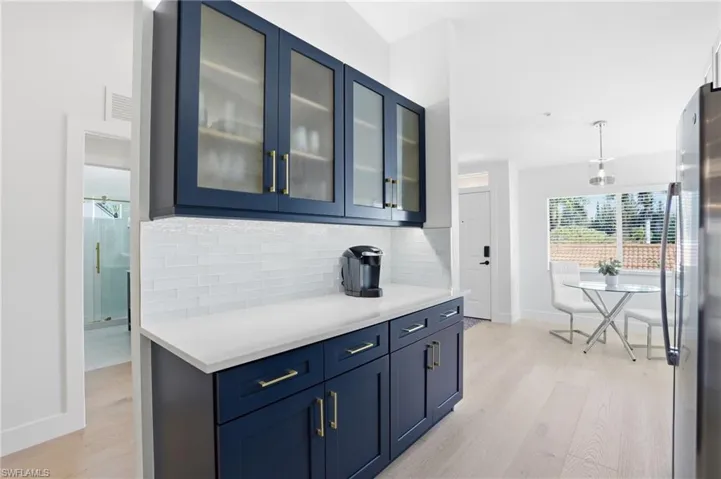 Bar area with blue cabinetry, glass fronted cabinets, freestanding refrigerator, and light wood finished floors