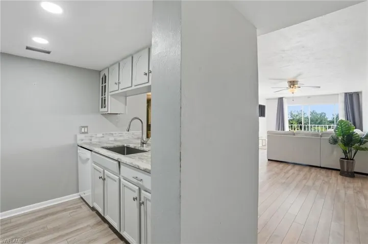 Kitchen with light wood-style flooring, white cabinets, light stone counters, ceiling fan, and open floor plan