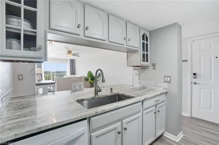 Kitchen with glass insert cabinets, light stone counters, dishwasher, light wood-style flooring, and a ceiling fan