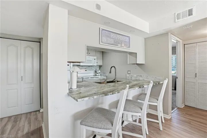 Kitchen with a kitchen bar, light wood-style flooring, white appliances, and decorative backsplash