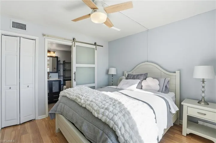 Bedroom featuring a barn door, light wood-type flooring, ensuite bathroom, and a closet