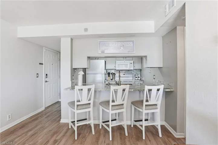 Kitchen featuring tasteful backsplash, white appliances, white cabinets, a breakfast bar, and light stone counters