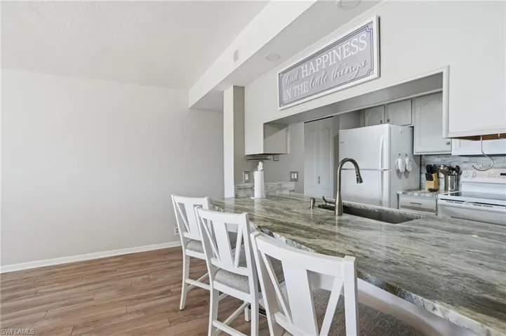 Kitchen with white appliances, light wood-style flooring, a breakfast bar area, tasteful backsplash, and dark stone counters