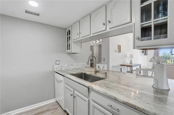 Kitchen with glass insert cabinets, white cabinets, light stone countertops, dishwasher, and light wood-type flooring