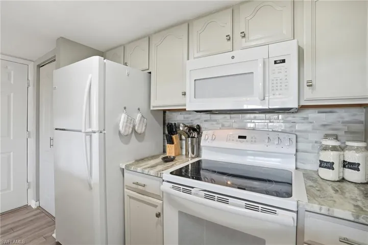 Kitchen with white appliances, light wood finished floors, white cabinetry, and decorative backsplash