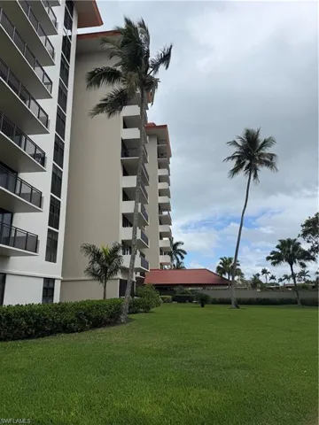 High-rise exterior featuring stacked private balconies with dark metal railings, red-tiled roof accents, and landscaped grounds with mature palm trees