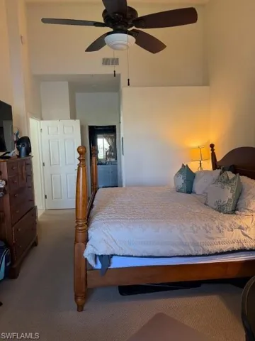 Carpeted bedroom featuring ceiling fan, a high ceiling, and ensuite bathroom