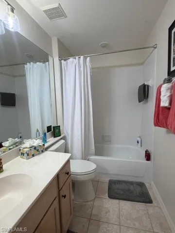Bathroom with vanity, shower / bathtub combination with curtain, and light tile patterned floors