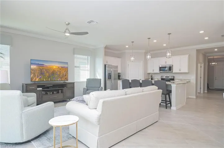 Living room with ceiling fan, light tile patterned flooring, crown molding, and sink