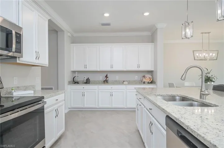 Kitchen featuring sink, white cabinetry, appliances with stainless steel finishes, decorative light fixtures, and light stone countertops