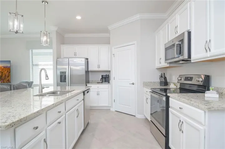 Kitchen featuring appliances with stainless steel finishes, white cabinets, a kitchen island with sink, ornamental molding, and sink