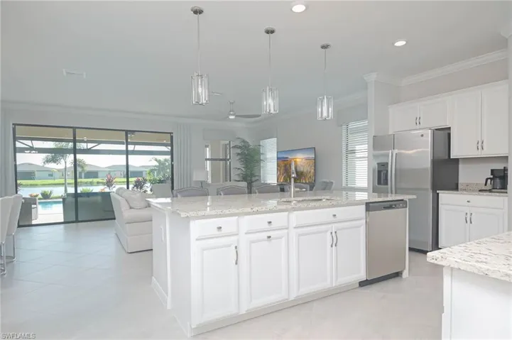 Kitchen featuring white cabinets, pendant lighting, a center island with sink, appliances with stainless steel finishes, and crown molding