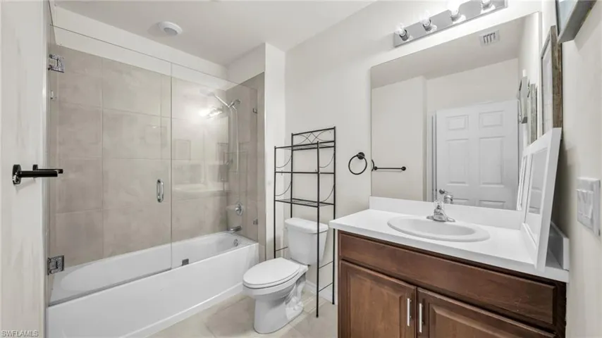 Bathroom featuring bath / shower combo with glass door, vanity, and light tile patterned flooring