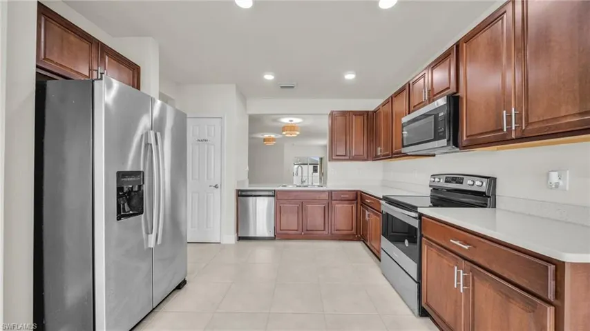 Kitchen with stainless steel appliances, light tile patterned floors, recessed lighting, brown cabinets, and light stone countertops