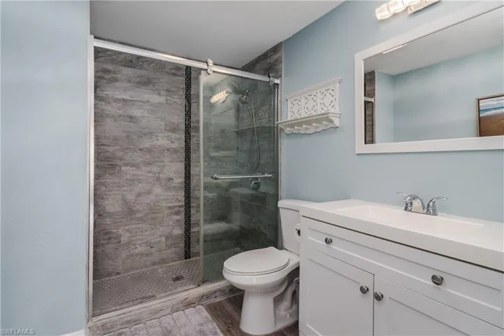 Full bathroom with vanity, a stall shower, wood laminate finished floors, and toilet