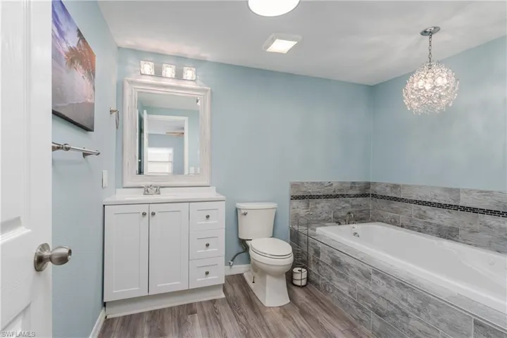 Full bath with a garden tub, toilet, wood finished floors, vanity, and baseboards