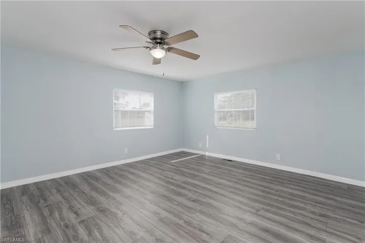 Unfurnished room featuring a healthy amount of sunlight, ceiling fan, baseboards, and wood finished floors