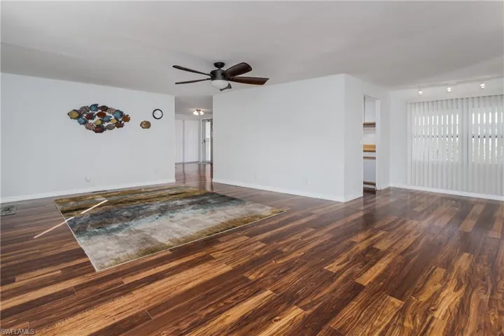 Unfurnished living room featuring ceiling fan, baseboards, and dark wood-style flooring