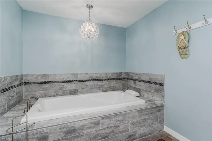 Full bath featuring baseboards, tiled tub, and a notable chandelier