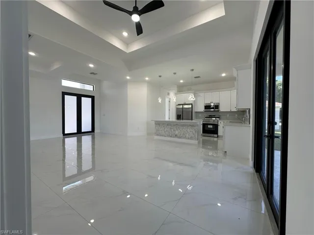 Unfurnished living room with a tray ceiling, recessed lighting, a ceiling fan, and marble finish floor