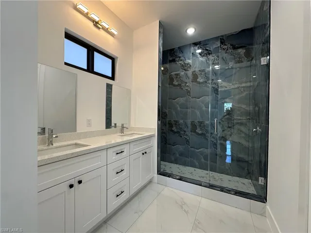 Bathroom featuring double vanity, marble finish floor, a marble finish shower, and a sink