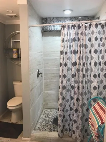 Bathroom with tile patterned floors, walk in shower, ornamental molding, and toilet
