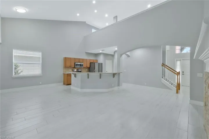 Living area featuring stairway, high vaulted ceiling, baseboards, arched walkways, and light wood-style floors