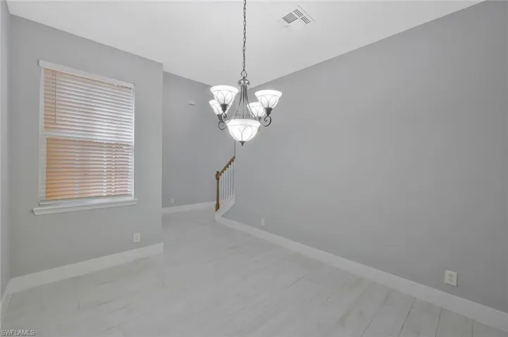Empty room with baseboards, a notable chandelier, visible vents, and light wood-type flooring