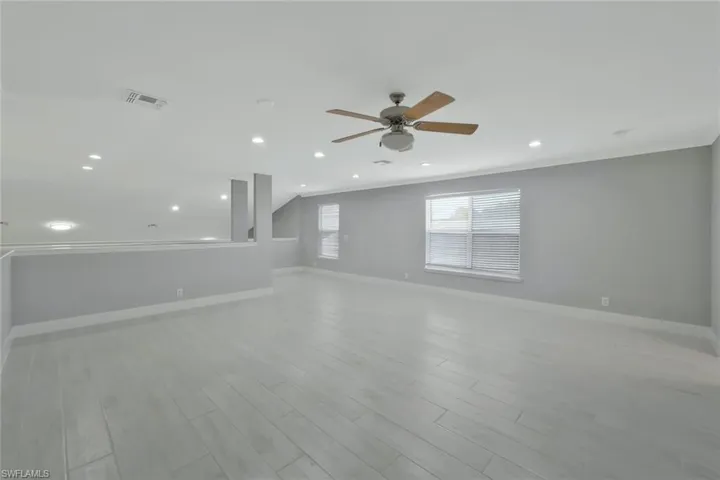 Empty room featuring light wood-style flooring, ornamental molding, baseboards, visible vents, and a ceiling fan