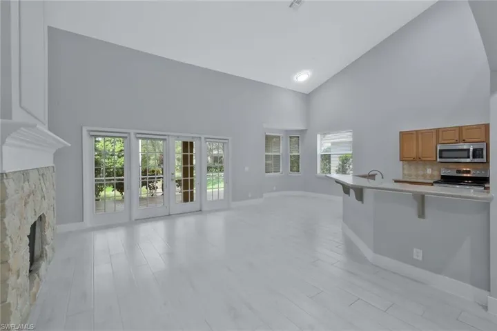 Unfurnished living room featuring baseboards, a fireplace, high vaulted ceiling, and light wood-style floors