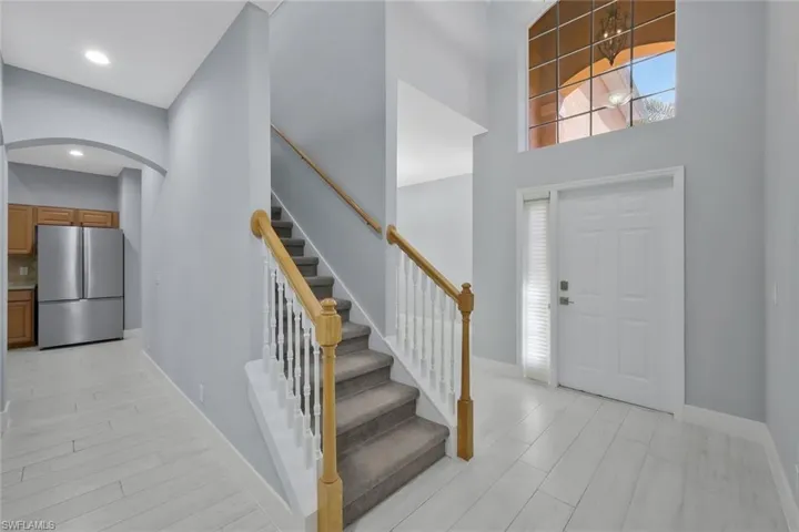 Entrance foyer with stairs, light wood-style flooring, baseboards, arched walkways, and a towering ceiling
