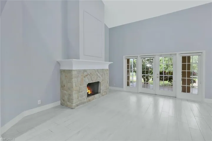 Unfurnished living room with baseboards, a towering ceiling, wood finished floors, and a stone fireplace